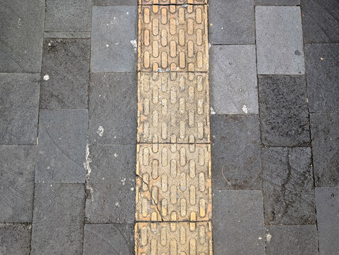 Texture of yellow tactile paving blocks on sidewalk pavement.