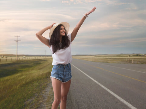 Woman in hat standing on a highway waving her hand to stop vehicle for a lift