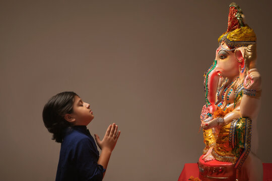 Kid praying with hands joined and eyes closed in front of Ganpati Idol.