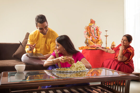 Husband wife sitting together while wife makes modaks and husband showing her laptop