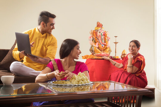 Husband wife sitting together while wife makes modaks and husband showing his mother laptop