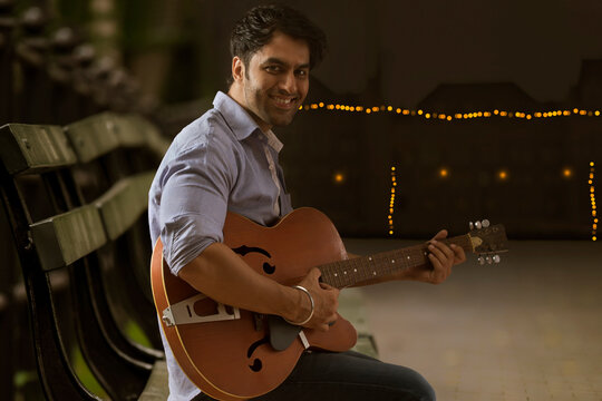 Young man sitting on Bench and playing guitar outdoors