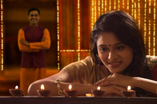 Woman decorating the house with diya on the occasion of diwali with husband standing in background