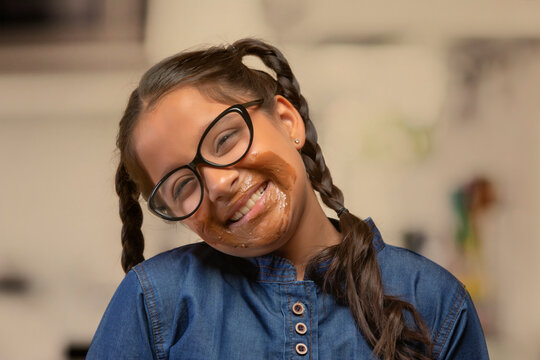 Portrait of a smiling girl in spectacles with chocolate marks around her mouth with head bent
