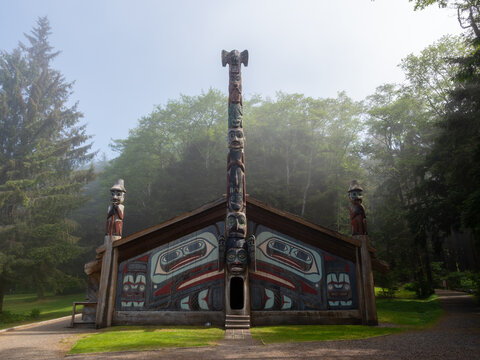 Ketchikan, Alaska, USA - June 1, 2022: Traditional indigenous carved longhouse with totem pole in Totem Bight Historic State Park on a foggy morning