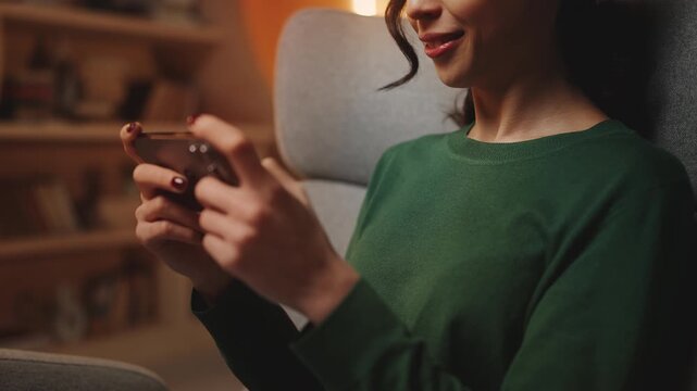 Positive young woman playing mobile video game in library, enjoying her hobby