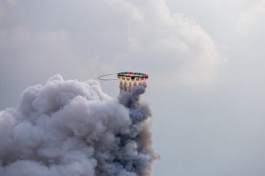 Circular traditional rocket launching into sky with massive white smoke clouds and fire jets