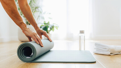 Fototapeta premium Yoga Mat Preparation: A person's hands are shown close-up as they neatly roll up a yoga mat on a wooden floor, ready for a session or put away after practice.