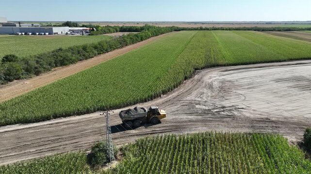 Drone aerial view of construction truck driving on partially built road. Highway infrastructure project with earthworks, soil compaction and gravel transport for modern civil engineering 