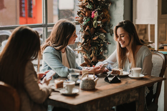 Three happy young women with cell phone meeting in a cafe