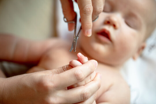 Mother carefully trimming fingernails of newborn baby with focused attention