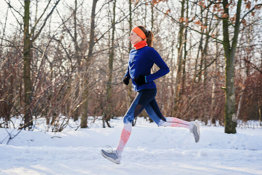 Woman running near bare trees during snow in winter