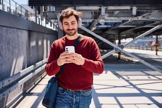 Person walking in urban parking lot using smartphone and headphones