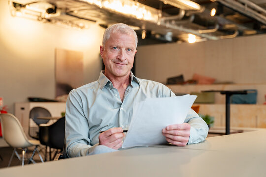 A smiling businessman holds a document in the office