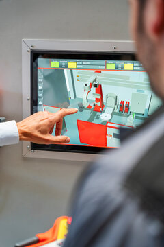A male engineer points at an industrial robot on a touchscreen