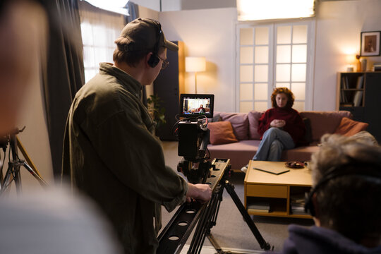 Cameraman films an actress on a living room set indoors