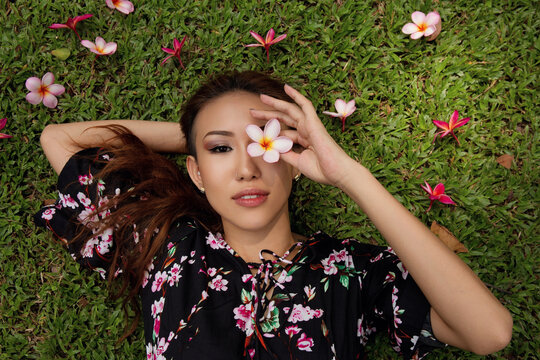 Model relaxing outdoors in a meadow holding a flower over the eye