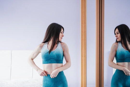 Sportswoman standing and looking in mirror at home
