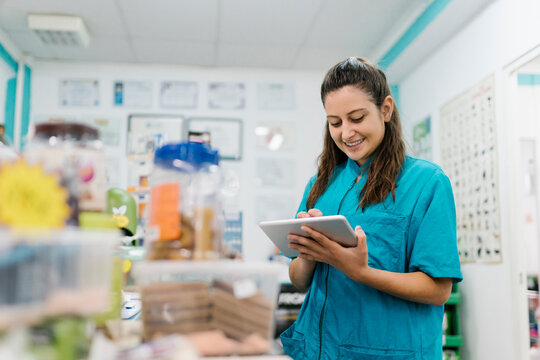 Smiling female groomer using digital tablet while standing in pet salon
