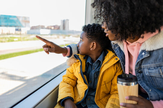 Mother sitting with son pointing through window in train