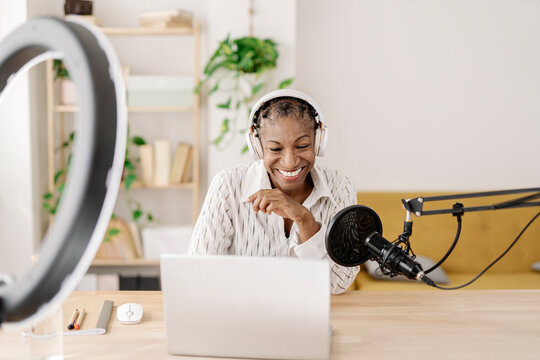 Smiling freelancer wearing wireless headphones recording podcast at table in home office