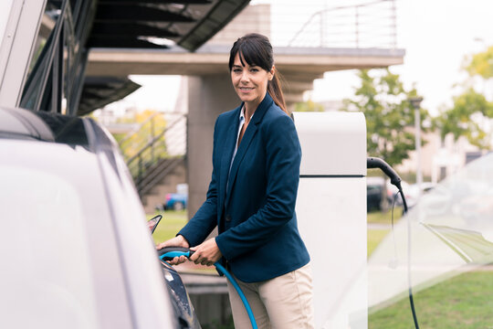 Smiling female entrepreneur plugging charger in electric car