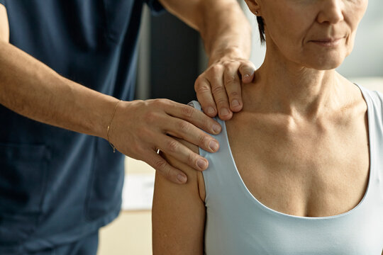 Physiotherapist examines shoulder of female patient in clinic