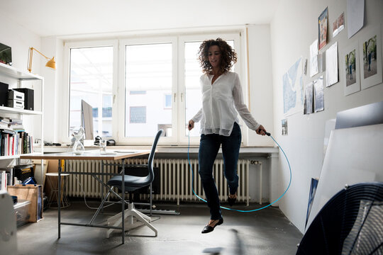 Businesswoman in office, training with skipping rope