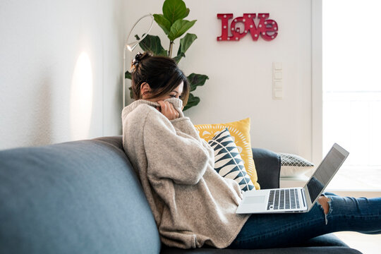 Woman sitting on her couch, surfing the net, using laptop