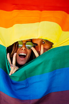 Two women looking through a crack in a rainbow flag