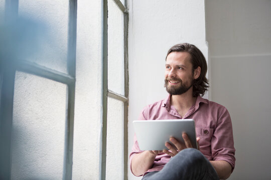 Man sitting on window sill using digital tablet