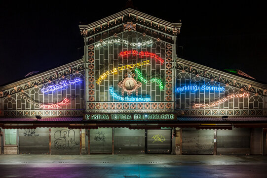 Torino, Italia - 13/12/2014 - Porta Palazzo. Facciata storica con orologio e installazione al neon multilingue. Scena urbana notturna ideale per architettura, arte pubblica e diversit&agrave; culturale.
