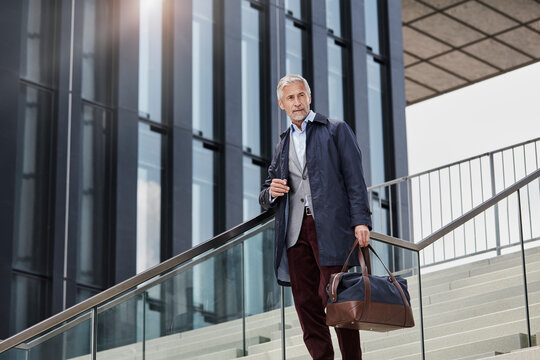 Portrait of mature businessman with traveling bag standing on stairs outdoors