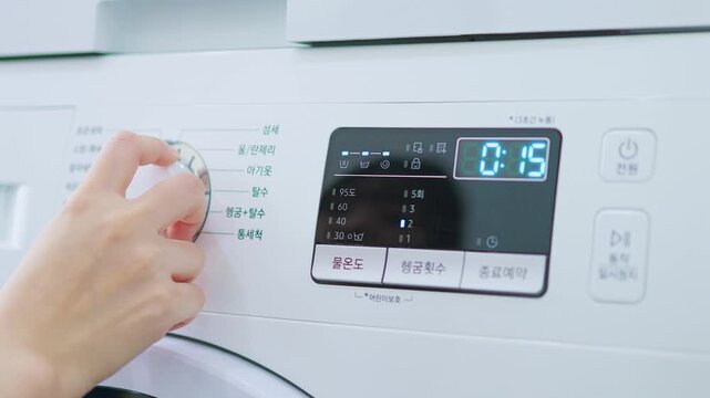 A close-up of a person's hand turning or pressing a dial on the control panel of a white washing machine.