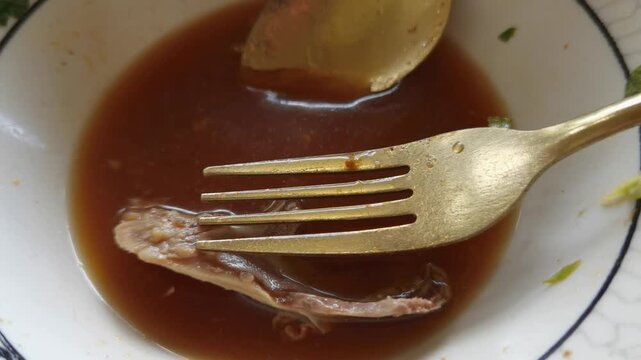 An empty bowl with remaining savory broth bone and golden fork spoon after finishing a meal