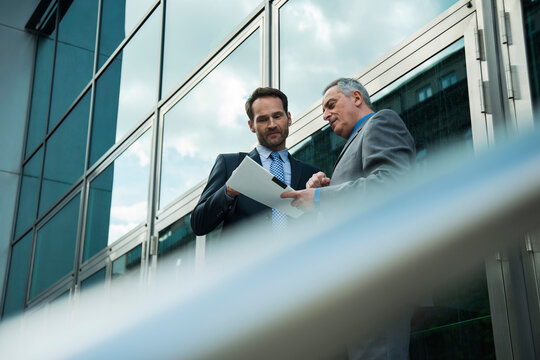 Two businessmen discussing documents outside office building