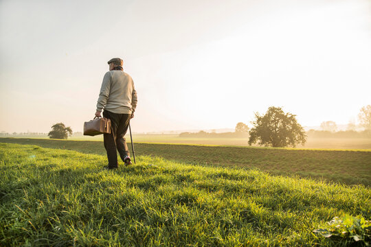 Senior man with bag walking in rural landscape