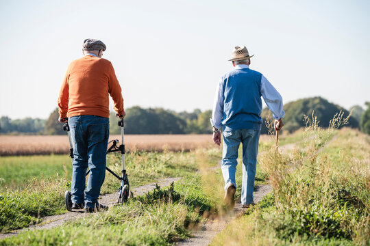 Old friends taking a stroll in the fields with walking stick and wheeled walker, talking about old times