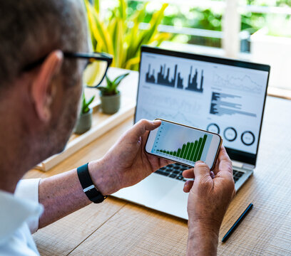 A man analyzes financial charts on his smartphone and laptop