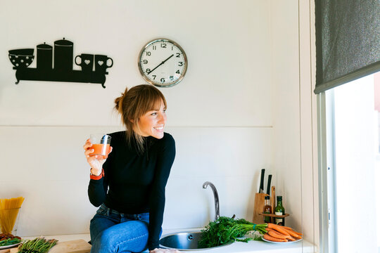 Young woman drinking fresh grapefruit juice in her kitchen
