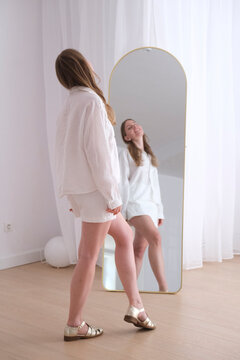 Model standing near mirror in casual white outfit smiling positively