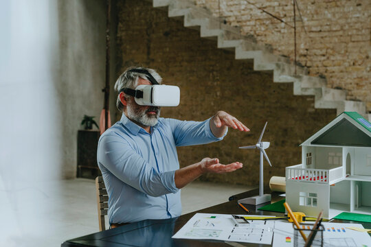 Businessman wearing VR simulator gesturing with model house on desk