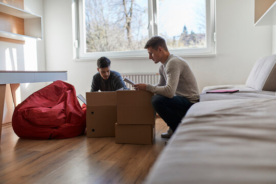 Two young men unpacking cardboard boxes in a room