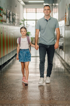 Father and daughter walking in school hallway holding hands