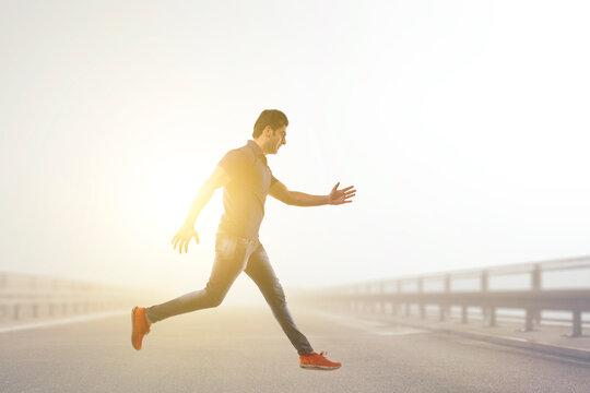 Young man leaping joyfully in mid air across the road with sun in the background.