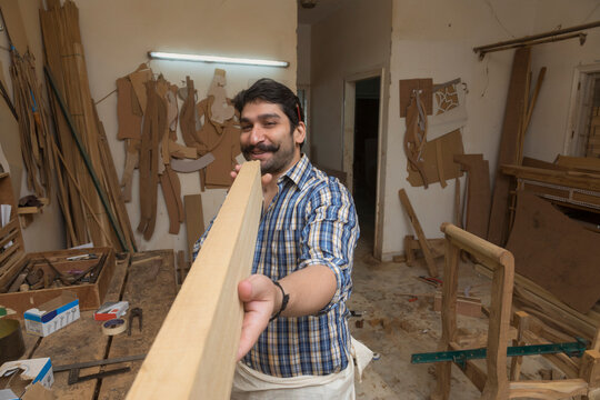 Happy looking carpenter in his workshop checking the straightness of a wooden log.