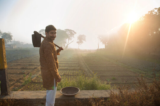 Happy looking farmer standing near his agriculture field with a spade and iron gold pan and sun in the background.