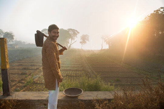 Smiling farmer standing near his agriculture field with a spade and iron gold pan and sun in the background.