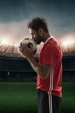 Football player kissing football with stadium in background
