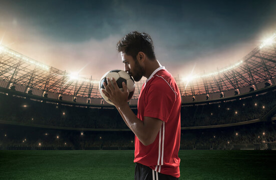 Football player kissing football with stadium in background